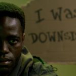 sad man sitting on the background of a sign saying i was downsized