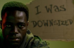 sad man sitting on the background of a sign saying i was downsized